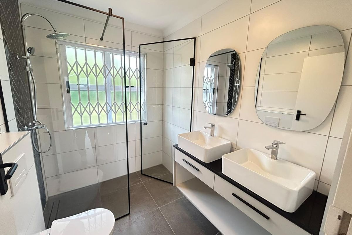 Modern bathroom featuring a double vanity with vessel sinks, a walk-in shower with glass screen, and contemporary wall-mounted toilet.