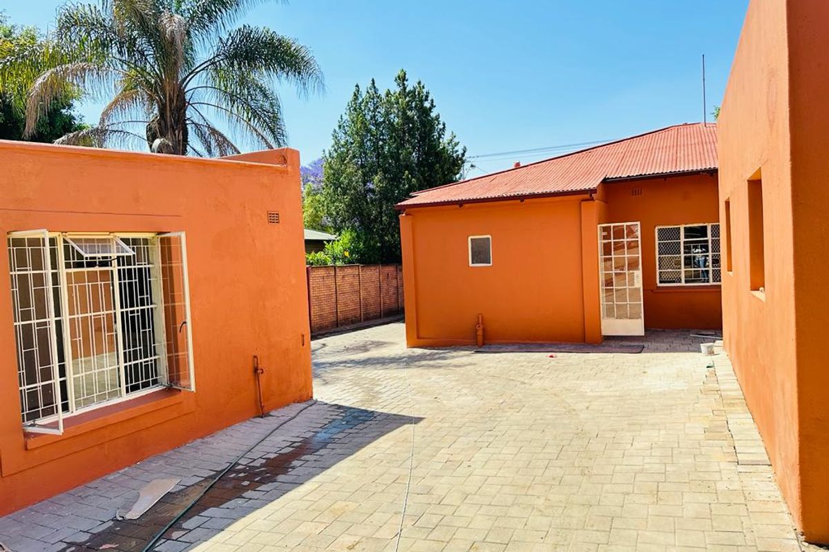 A view of the rear courtyard area featuring paved flooring and orange-painted exterior walls with security bars on the windows.
