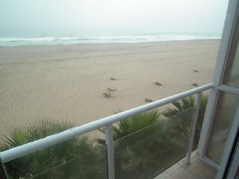 A direct ocean view from a balcony featuring a white metal railing and glass balustrade overlooking the sandy beach.