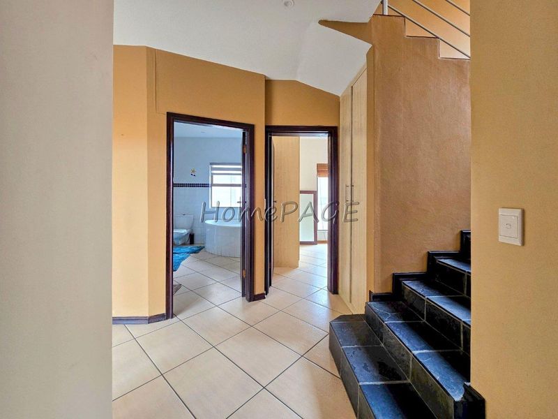 A tiled hallway featuring built-in storage cupboards and a staircase with stone treads, providing access to adjacent rooms.