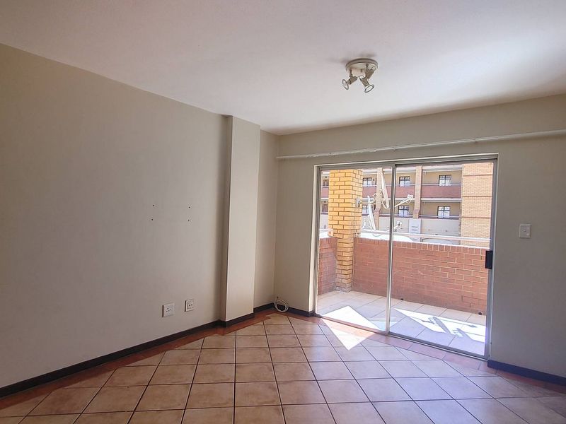 An empty living room featuring ceramic floor tiles and a sliding glass door providing access to a private balcony.
