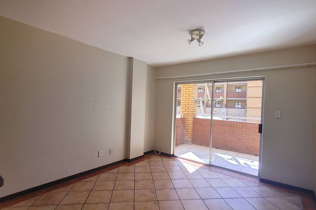 An empty living room featuring ceramic floor tiles and a sliding glass door providing access to a private balcony.