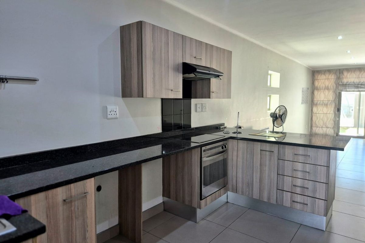 Modern kitchen featuring wood-grain cabinetry, granite countertops, integrated oven and hob, and tiled flooring in an open-plan layout.