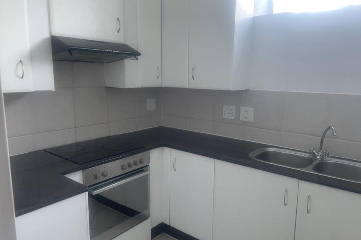 A functional kitchen featuring white cabinetry, dark countertops, a built-in oven with electric hob, extractor fan, and a double sink with tiled backsplash.