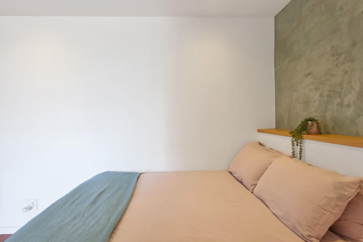 A modern bedroom featuring a textured accent wall, integrated timber shelving, and recessed downlighting.