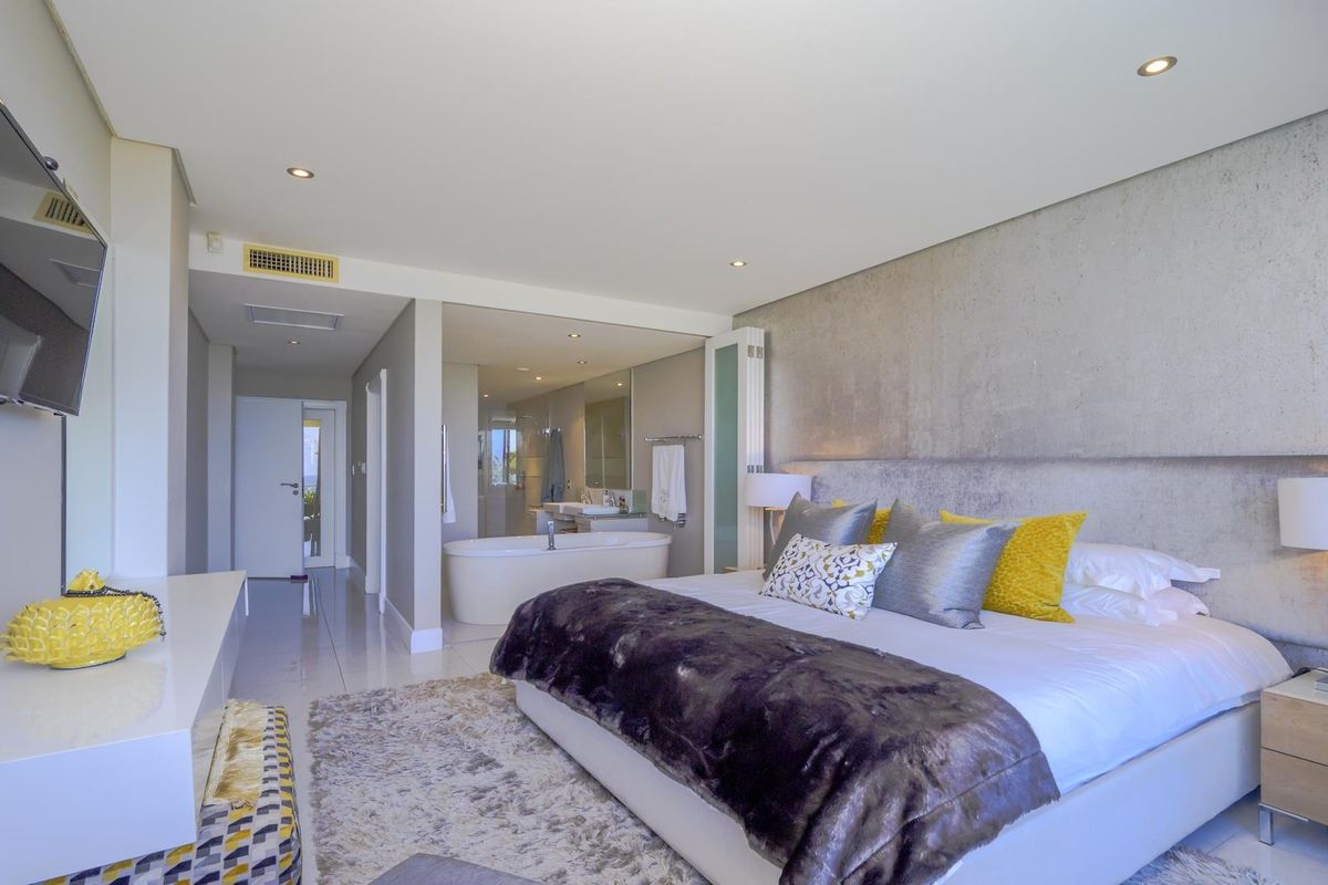 Modern bedroom featuring a concrete accent wall, tiled flooring, recessed lighting, and an open-plan en-suite bathroom with a freestanding bathtub.