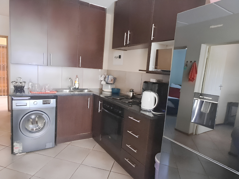 Functional kitchen featuring dark wood cabinetry, granite countertops, built-in oven, hob, and integrated laundry space, with direct access to an exterior security gate.