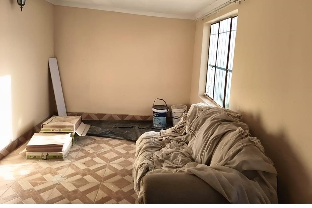 A small, unfinished room featuring tiled flooring and a window with security bars, currently used as a storage space for renovation materials.