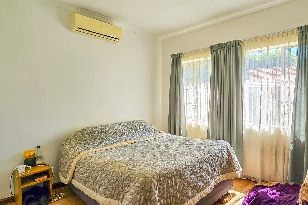 A bedroom featuring timber flooring and a wall-mounted split-system air conditioning unit, with natural light provided by large windows.