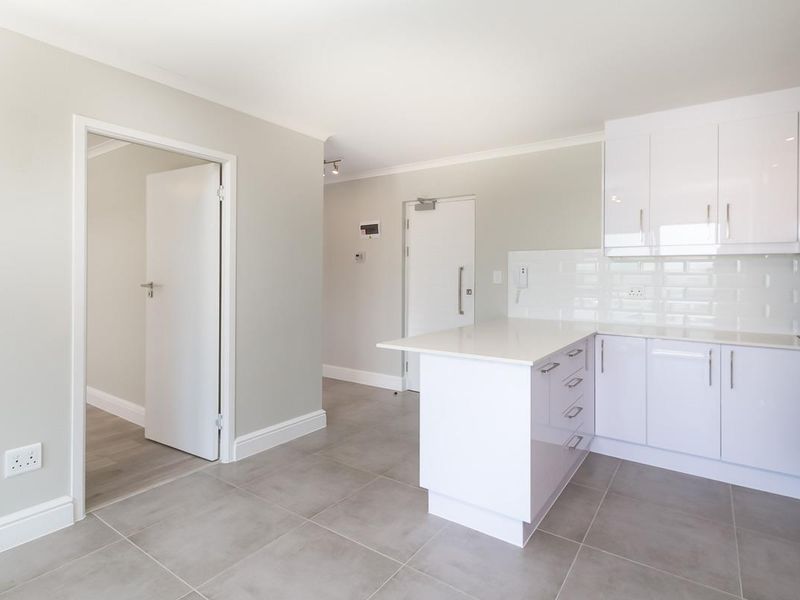 Modern kitchen featuring white gloss cabinetry, stone countertops, subway tile backsplash, and integrated appliances with neutral porcelain floor tiles.