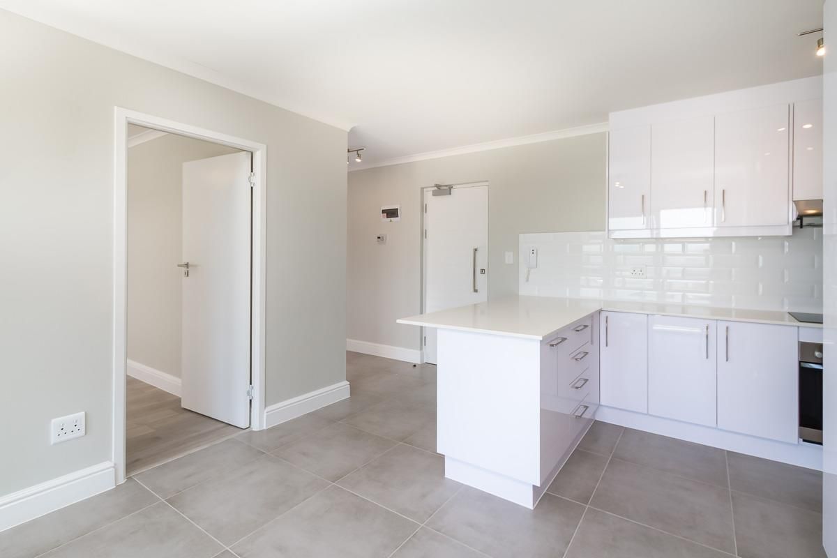 Modern kitchen featuring white gloss cabinetry, stone countertops, subway tile backsplash, and integrated appliances with neutral porcelain floor tiles.