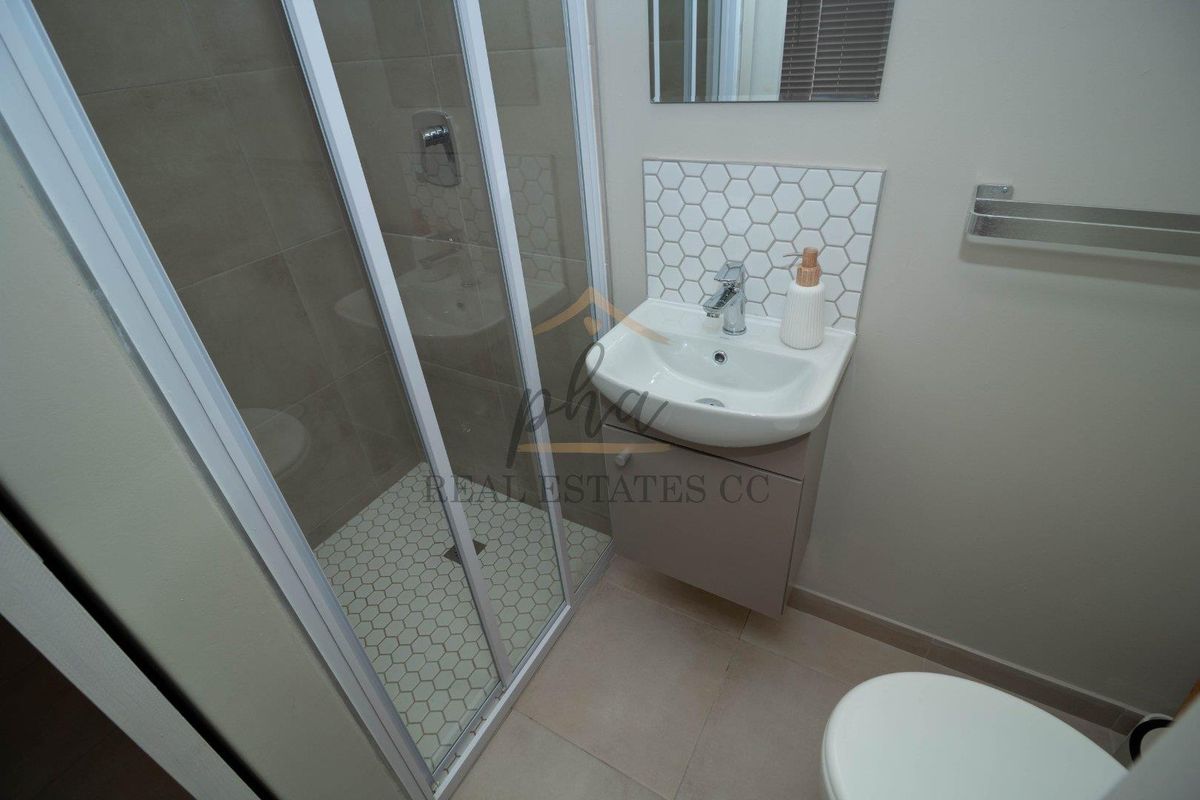 A modern bathroom featuring a glass-enclosed shower with mosaic floor tiles, a wall-mounted vanity with a basin, and a toilet.