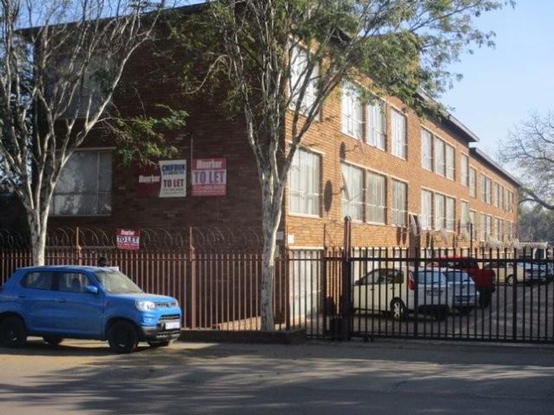 Exterior view of a multi-story brick apartment building featuring secure perimeter fencing and gated access.