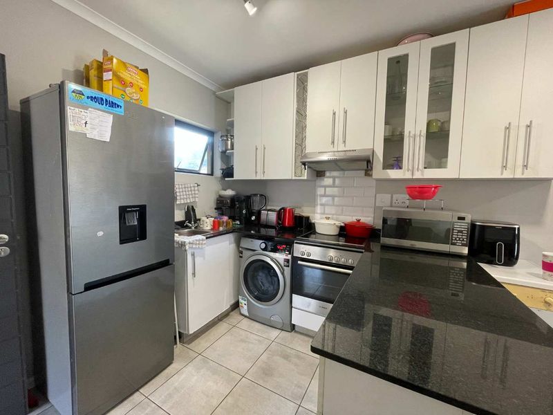 Compact kitchen featuring white cabinetry, granite countertops, subway tile backsplash, and integrated appliances including an oven, hob, and washing machine.