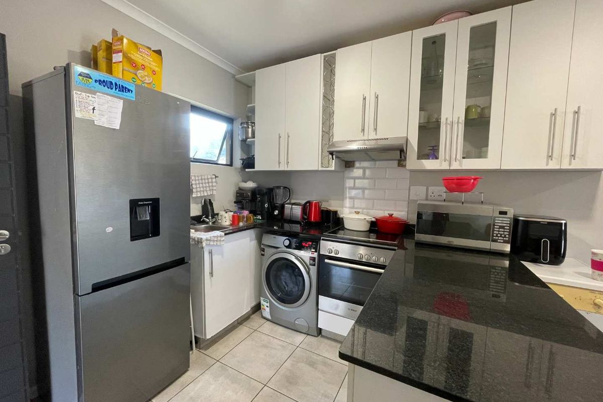Compact kitchen featuring white cabinetry, granite countertops, subway tile backsplash, and integrated appliances including an oven, hob, and washing machine.