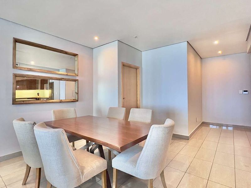 A bright and well-maintained dining area featuring neutral tiled flooring, recessed downlighting, and a clean, modern aesthetic.
