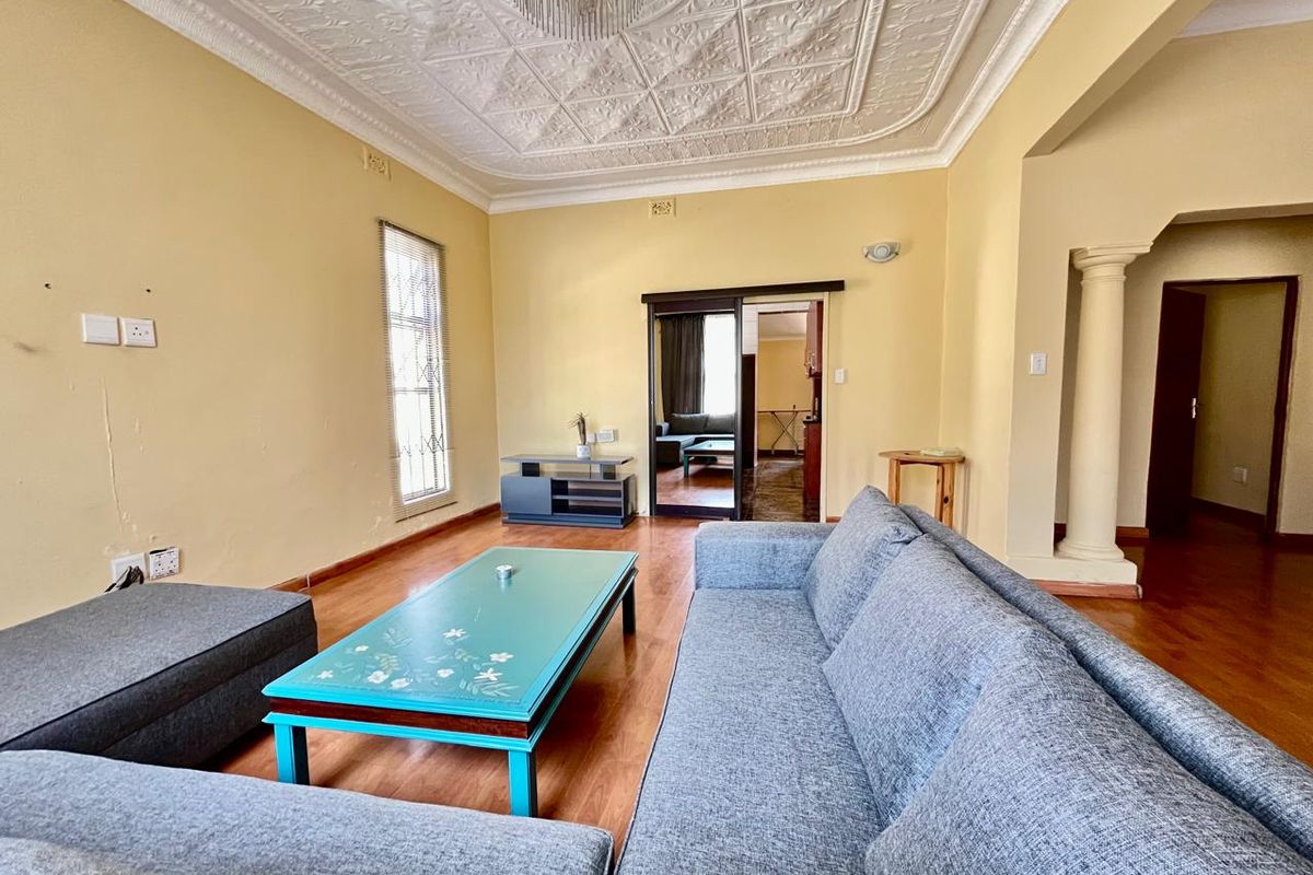 Spacious living room featuring decorative pressed metal ceiling, timber flooring, and a classic architectural column leading to an adjacent room.
