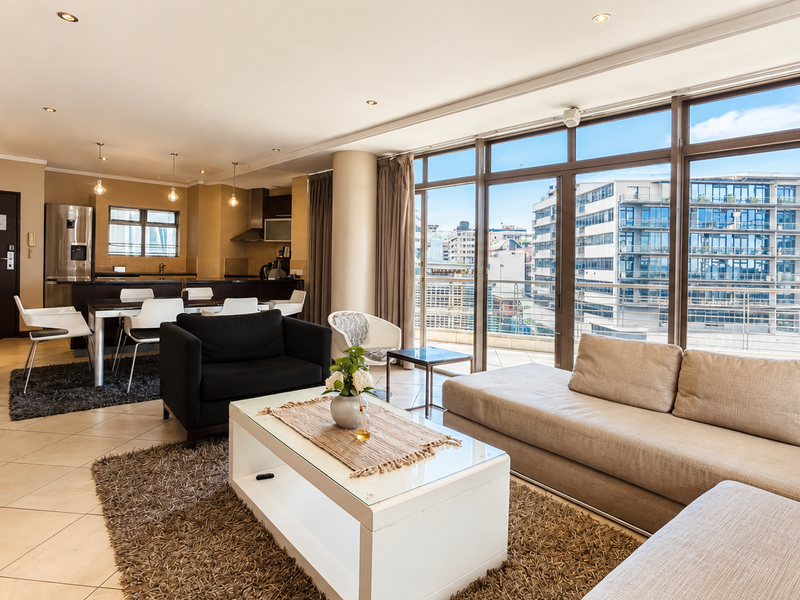 Spacious open-plan living and kitchen area featuring tiled floors, modern cabinetry, and large glass doors leading to a balcony with urban views.