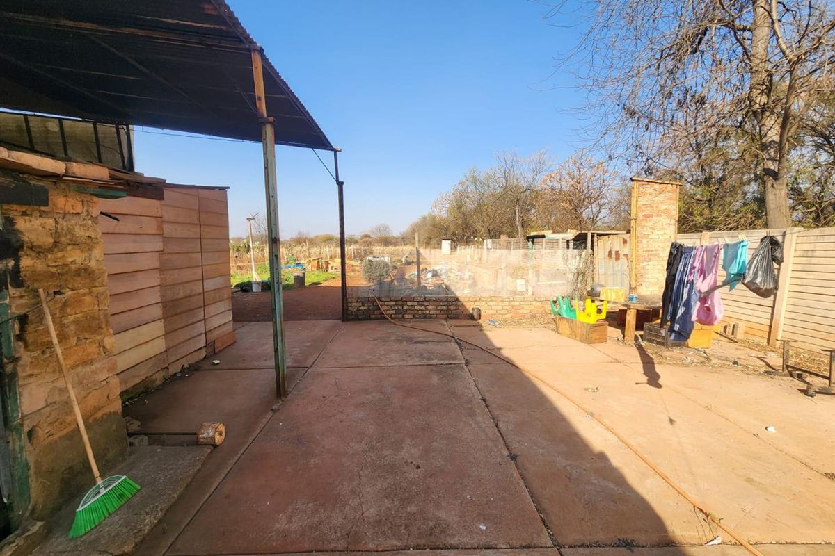 Rear outdoor area featuring a concrete patio, metal roof structure, and brick chimney, overlooking a fenced yard with natural surroundings.