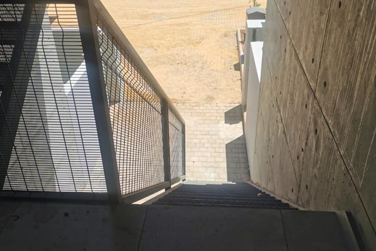 An exterior view looking down a metal staircase towards a paved courtyard area within an apartment complex.