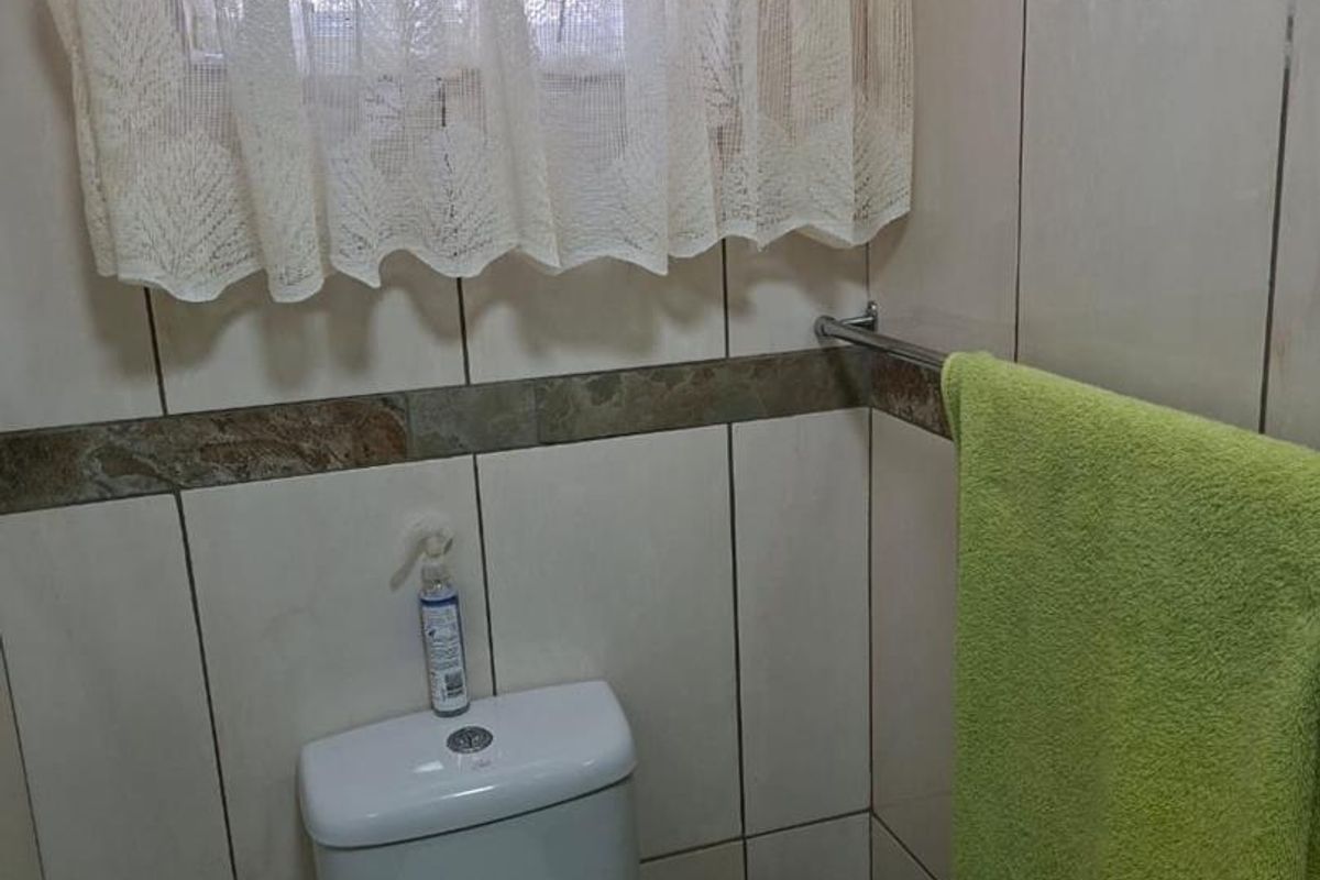 A functional bathroom featuring full-height ceramic wall tiles with a decorative border, a standard toilet, and a wall-mounted towel rail.