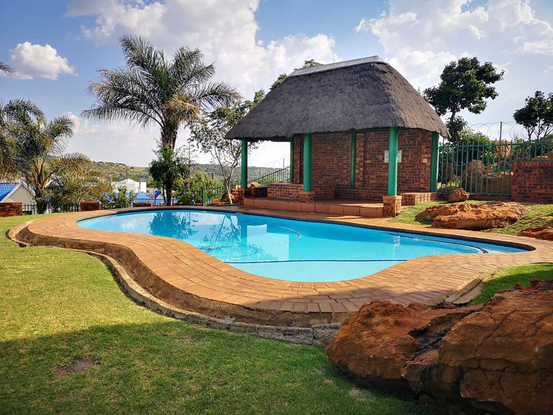 Outdoor pool area featuring a swimming pool, brick paved surround, and a thatched roof lapa set within a landscaped garden.