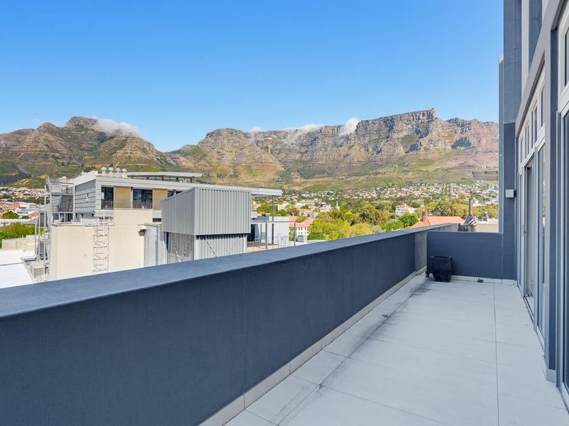Spacious penthouse balcony featuring tiled flooring and a solid balustrade, offering expansive, unobstructed views of the surrounding mountain range and cityscape.