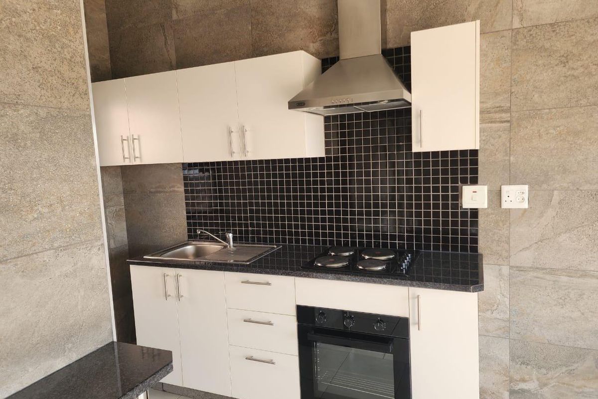 Modern kitchen featuring white cabinetry, black mosaic tile backsplash, built-in oven, hob, and stainless steel extractor fan against stone-tiled walls.