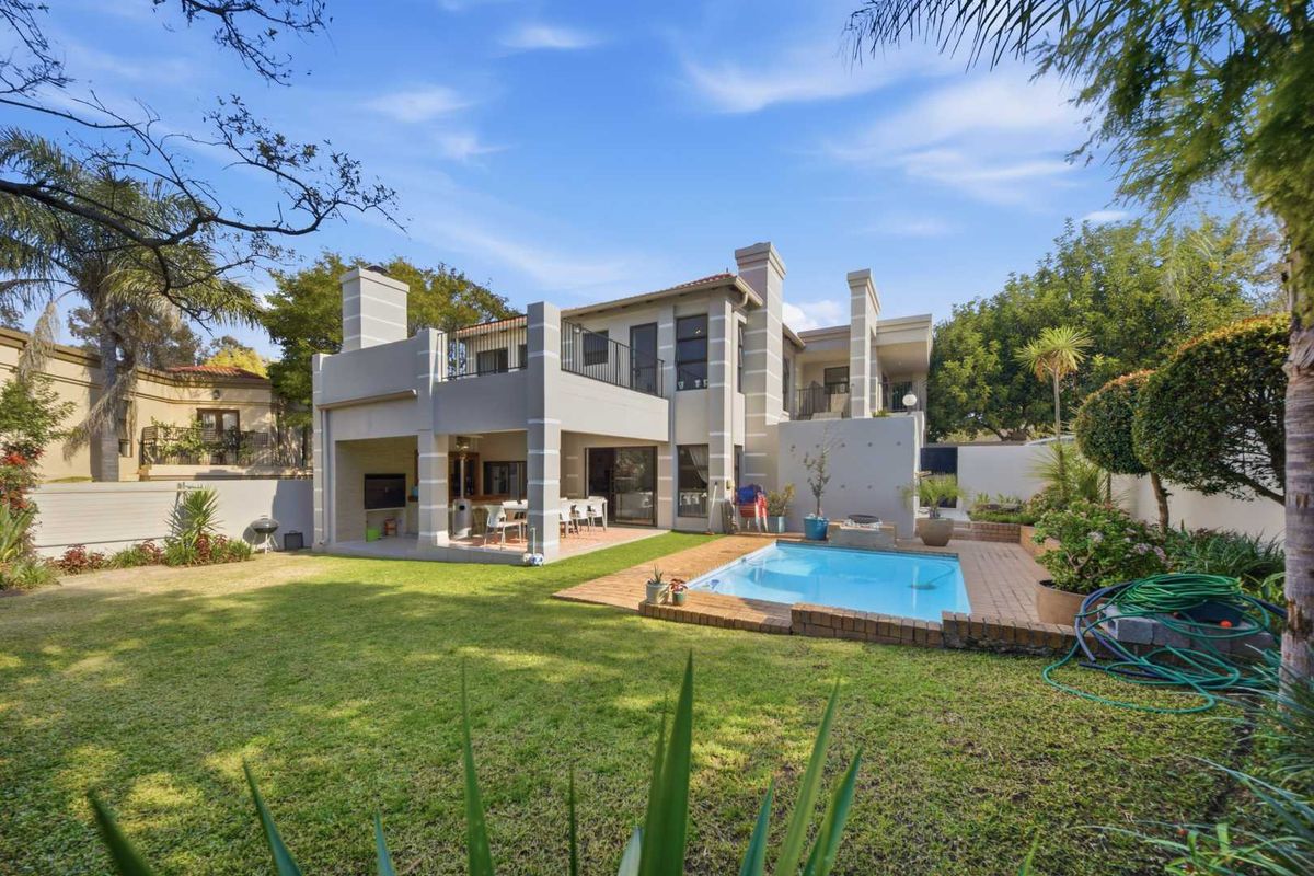 Rear view of the property featuring a swimming pool, landscaped garden, and a covered patio area with an upper-level balcony.