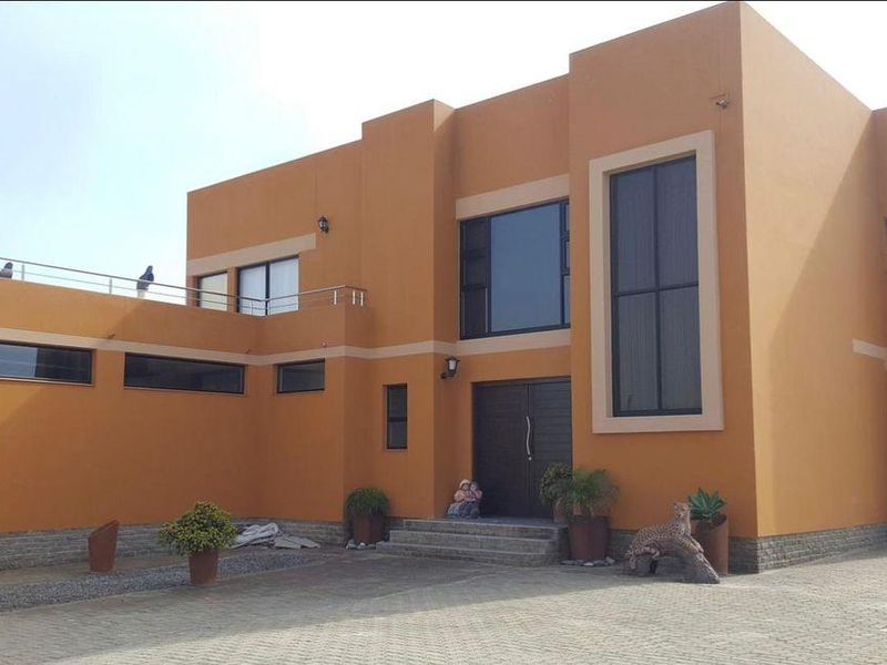 Modern two-story house exterior featuring a bold orange facade, stone cladding accents, a paved driveway, and a double garage.