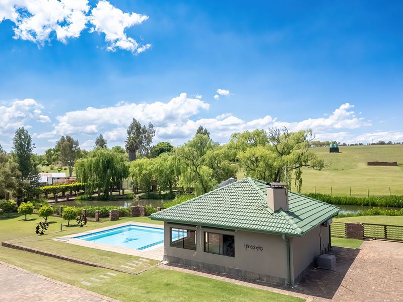 Aerial view of a well-maintained property featuring a swimming pool, a detached structure with a tiled roof, and expansive landscaped grounds.