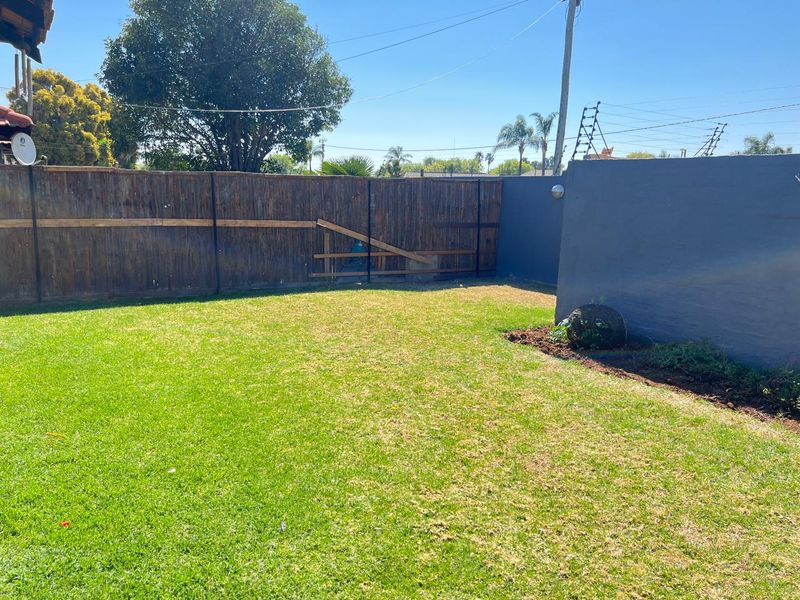 A private rear garden featuring a well-maintained lawn, enclosed by a combination of wooden fencing and a painted masonry boundary wall.