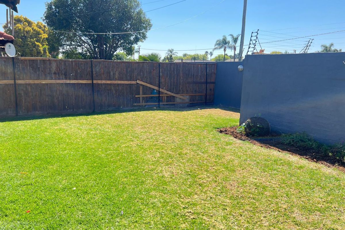 A private rear garden featuring a well-maintained lawn, enclosed by a combination of wooden fencing and a painted masonry boundary wall.