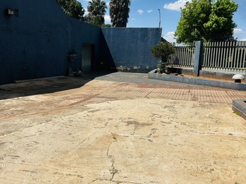 Spacious exterior driveway area featuring concrete and brick paving, enclosed by a perimeter wall with security fencing.