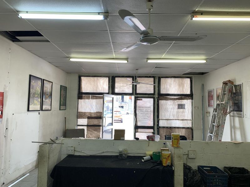 Open-plan retail space featuring a suspended ceiling, fluorescent lighting, and a partition wall, currently in need of cosmetic refurbishment.