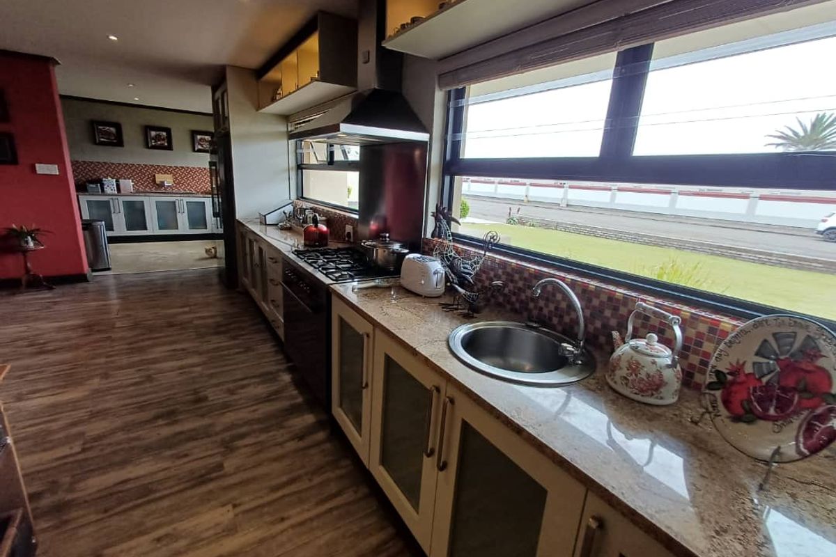 A well-appointed kitchen featuring granite countertops, a gas hob with extractor fan, stainless steel sink, and ample cabinetry with a view of the exterior.