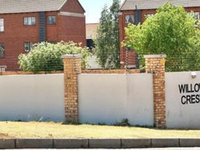 Street view of the Willow Crest apartment complex entrance, featuring a brick boundary wall with integrated electric fencing.