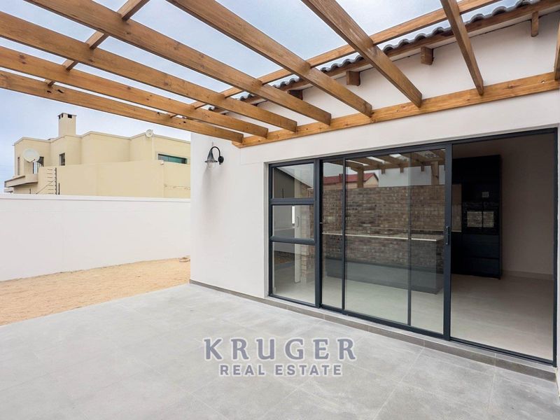 A modern covered patio featuring a timber pergola, tiled flooring, and large sliding glass doors providing seamless access to the interior living space.