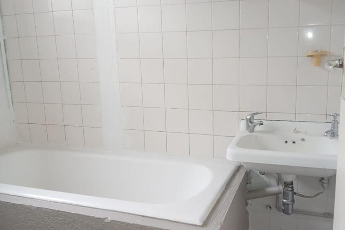 A dated bathroom featuring a standard bathtub, wall-mounted basin, and tiled splashbacks, currently requiring significant renovation and cosmetic updates.