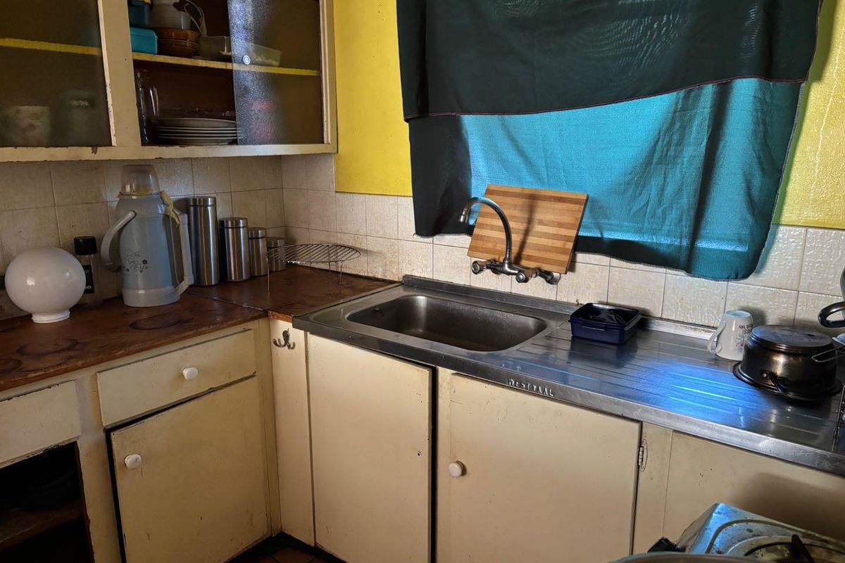 A dated kitchen featuring original cabinetry, a stainless steel sink, and tiled backsplash, requiring modernization to improve functionality and aesthetic appeal.