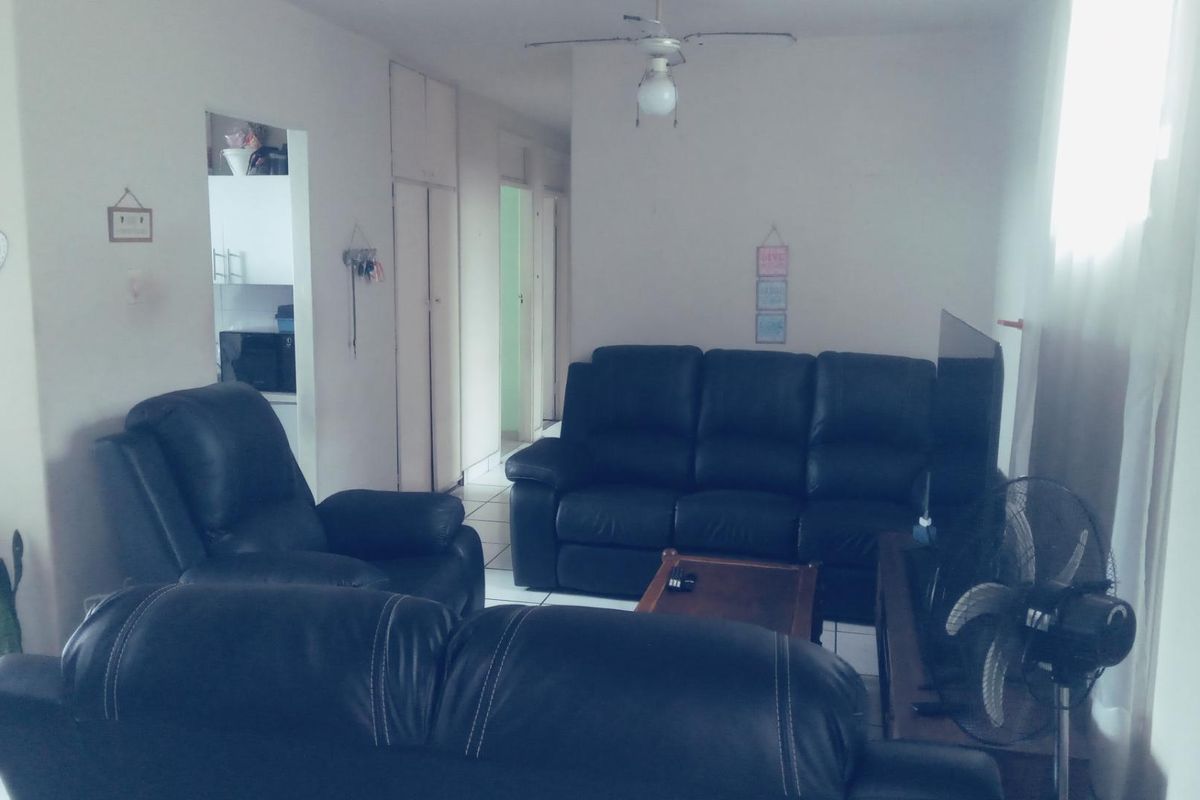 A living room area featuring tiled flooring, built-in storage cupboards, and a ceiling fan, with an adjacent view into the kitchen area.