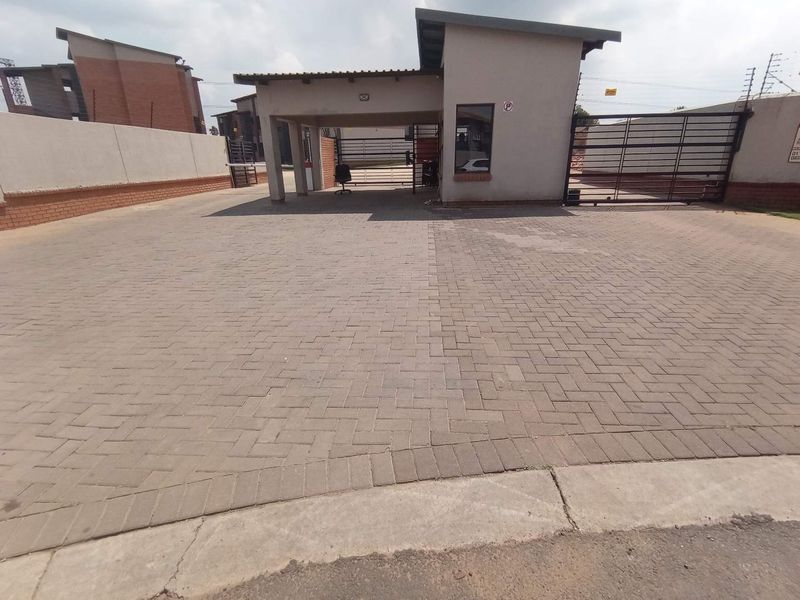The property entrance features a paved driveway leading to a security guard house, enclosed by perimeter walls with electric fencing and a metal gate.