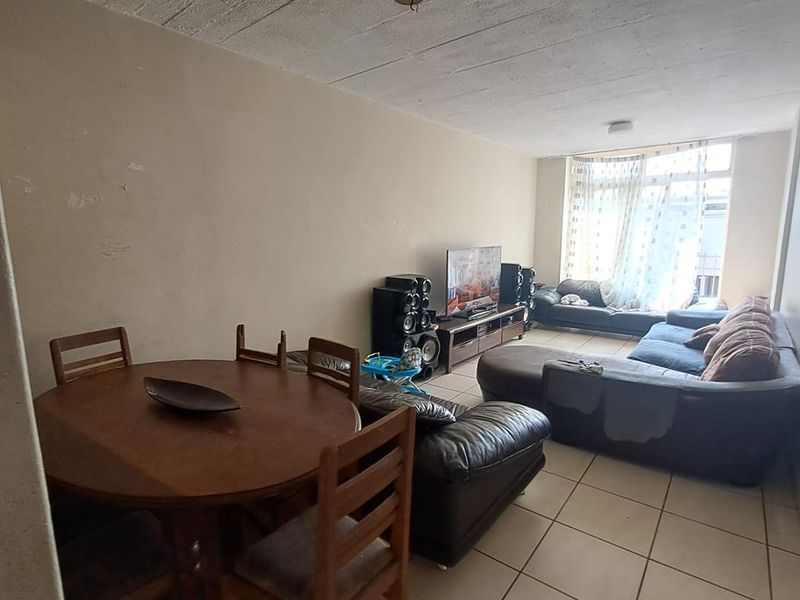 Open-plan living and dining area featuring tiled flooring and an exposed concrete ceiling, requiring cosmetic updates to the wall finishes.