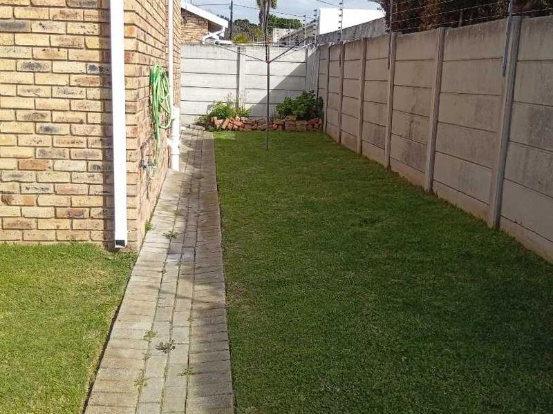 A side garden area featuring a paved walkway, lawn, and secure precast concrete boundary wall with electric fencing.