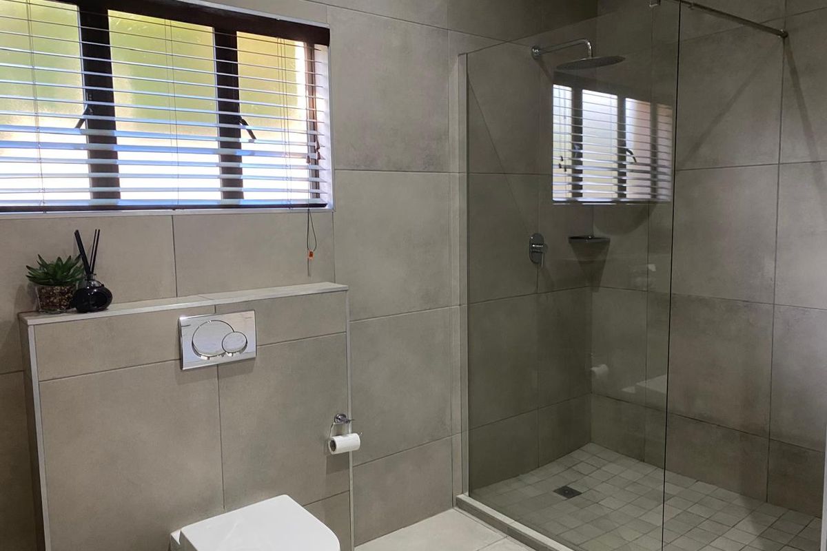 Modern bathroom featuring large-format grey wall tiles, a walk-in shower with a frameless glass screen, and a wall-hung toilet with a concealed cistern.