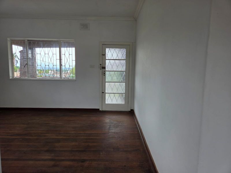 An empty living room featuring original hardwood flooring, a textured glass exterior door, and windows fitted with security bars.
