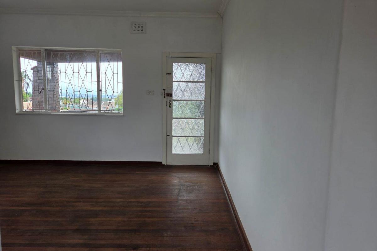 An empty living room featuring original hardwood flooring, a textured glass exterior door, and windows fitted with security bars.