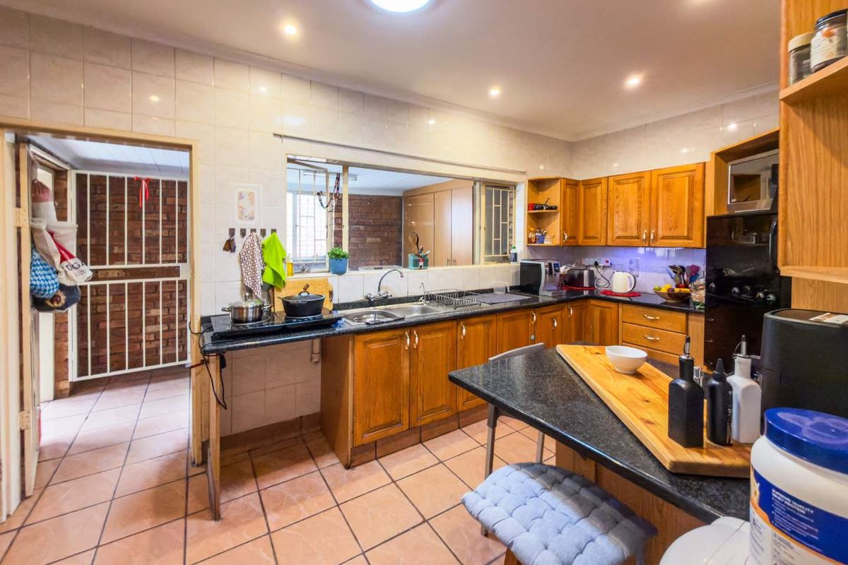 Functional kitchen featuring wooden cabinetry, granite countertops, tiled flooring, and a convenient serving hatch connecting to the adjacent living area.