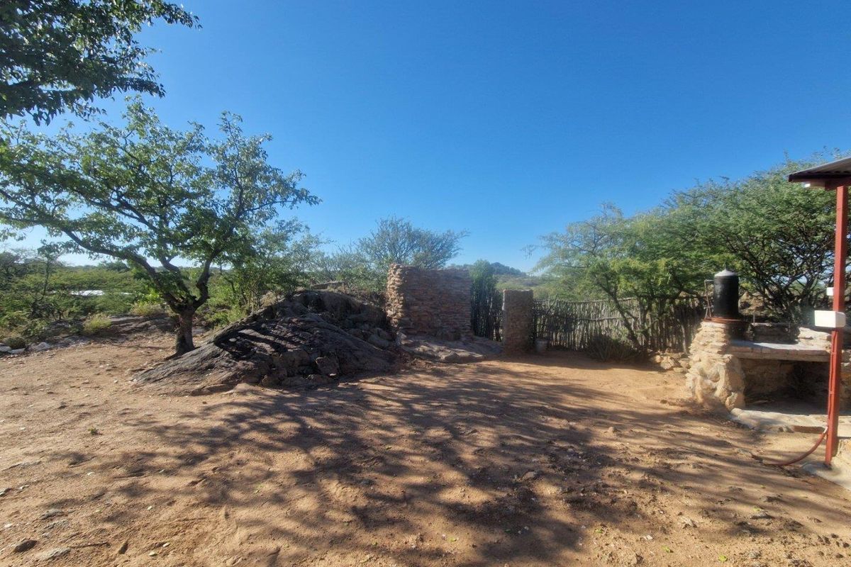 Outdoor lodge area featuring a rustic stone braai or fireplace structure set within a natural, undeveloped landscape.