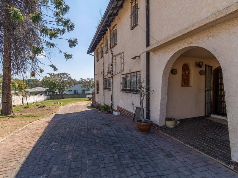 Side view of the property featuring a paved driveway, arched entrance, and stucco exterior with security bars on windows.